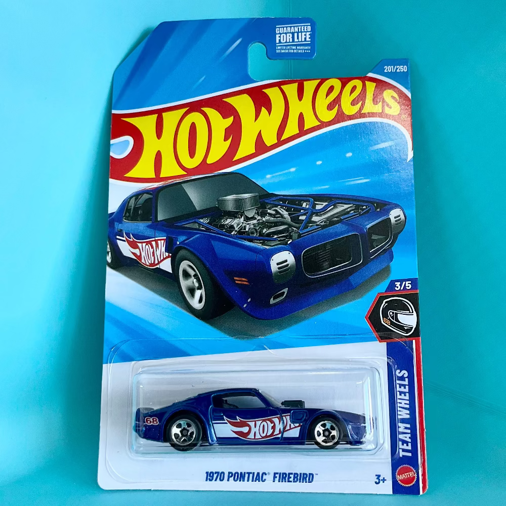 A Hot Wheels Team Wheels 1/5 scale die-cast model car of a 1970 Pontiac Firebird, shown in its original blue and white blister card packaging against a bright cyan background.