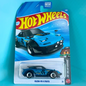 A Hot Wheels Mazda MX-5 Miata die-cast toy car in its original blister card packaging, set against a solid turquoise background.