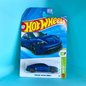 A Hot Wheels Porsche Taycan Turbo S die-cast toy car in its original blister card packaging, set against a bright cyan background.