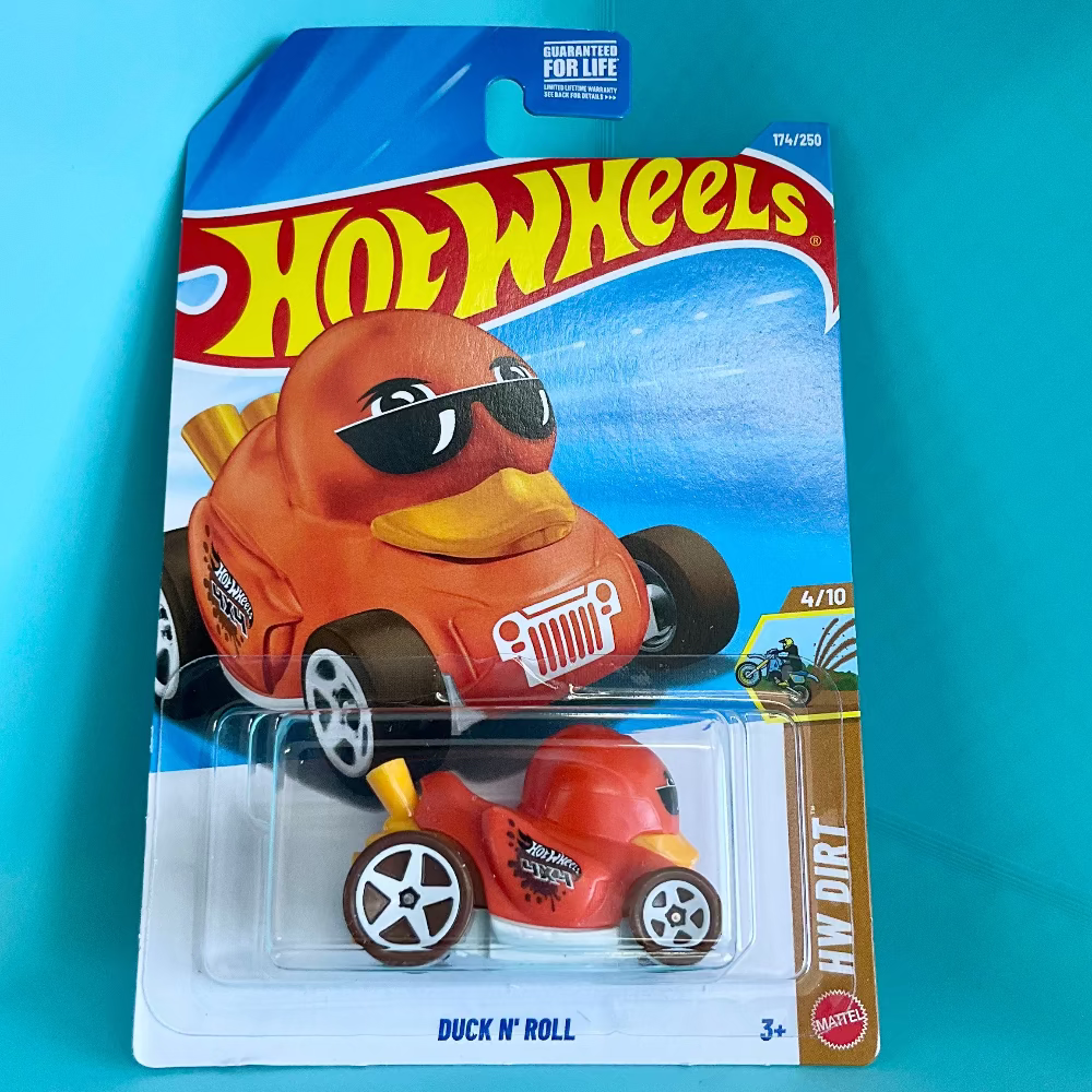 A Hot Wheels 'Duck 'N' Roll' toy car in its original blister card packaging, set against a bright turquoise background. The toy is an orange duck-themed race car with a yellow beak and black sunglasses.