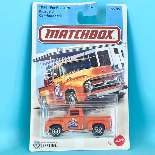 A Matchbox die-cast toy truck in its original blister card packaging, featuring a 1956 Ford F-100 Pickup. The toy truck is orange with a cartoon graphic on the side door, and the packaging displays an illustration of the full truck.